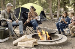 mother, father, and two kids sitting around a campfire with Coleman Camping Equipment